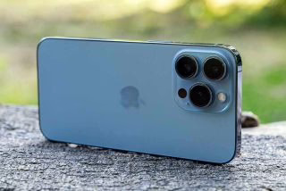 iPhone 13 Pro Max in blue color showcasing its triple-camera system and Apple logo, emphasizing its premium design and features in a review context.