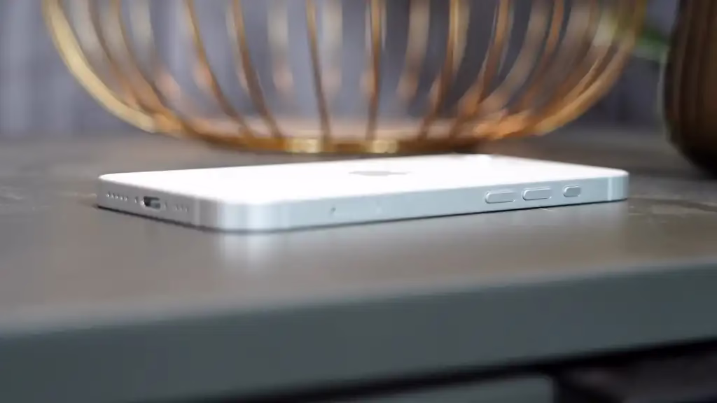 Used iPhone 16e lying on a table, showcasing its sleek design and camera features, with a decorative bowl in the background.