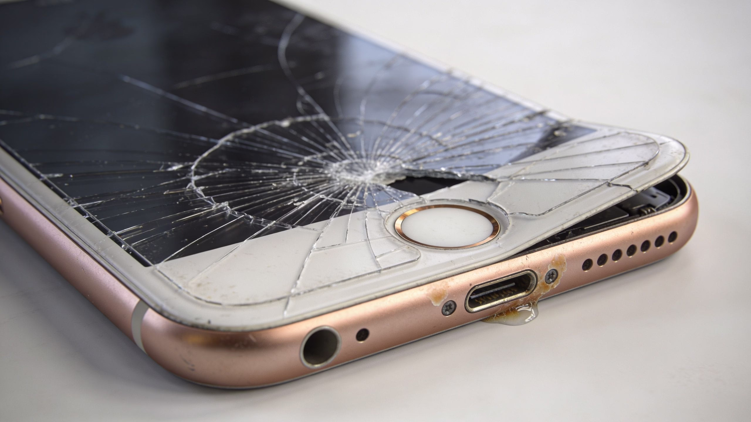 How to Repair Broken iPhone Screen 3 A rose gold iPhone with a severely shattered screen and visible liquid damage near the charging port.