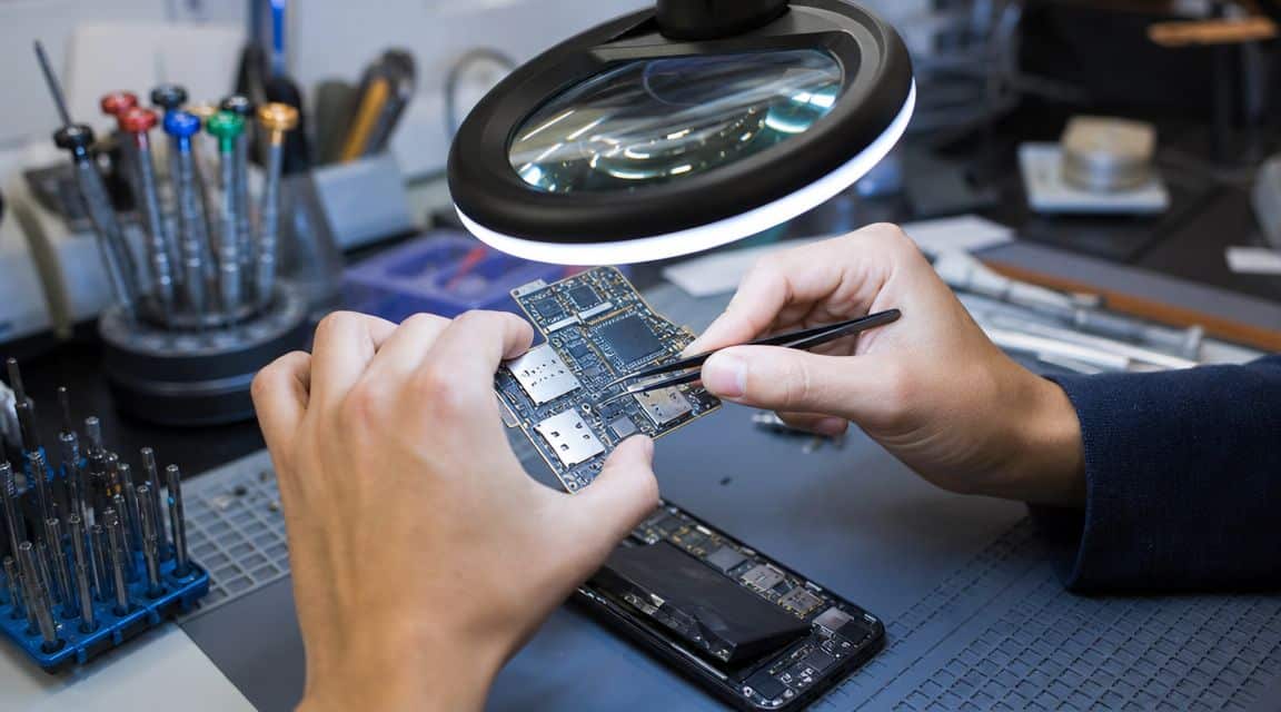 Are Refurbished Phones Safe UK 2 A technician using tweezers to perform delicate repairs on a smartphone motherboard under a lighted magnifying lamp.