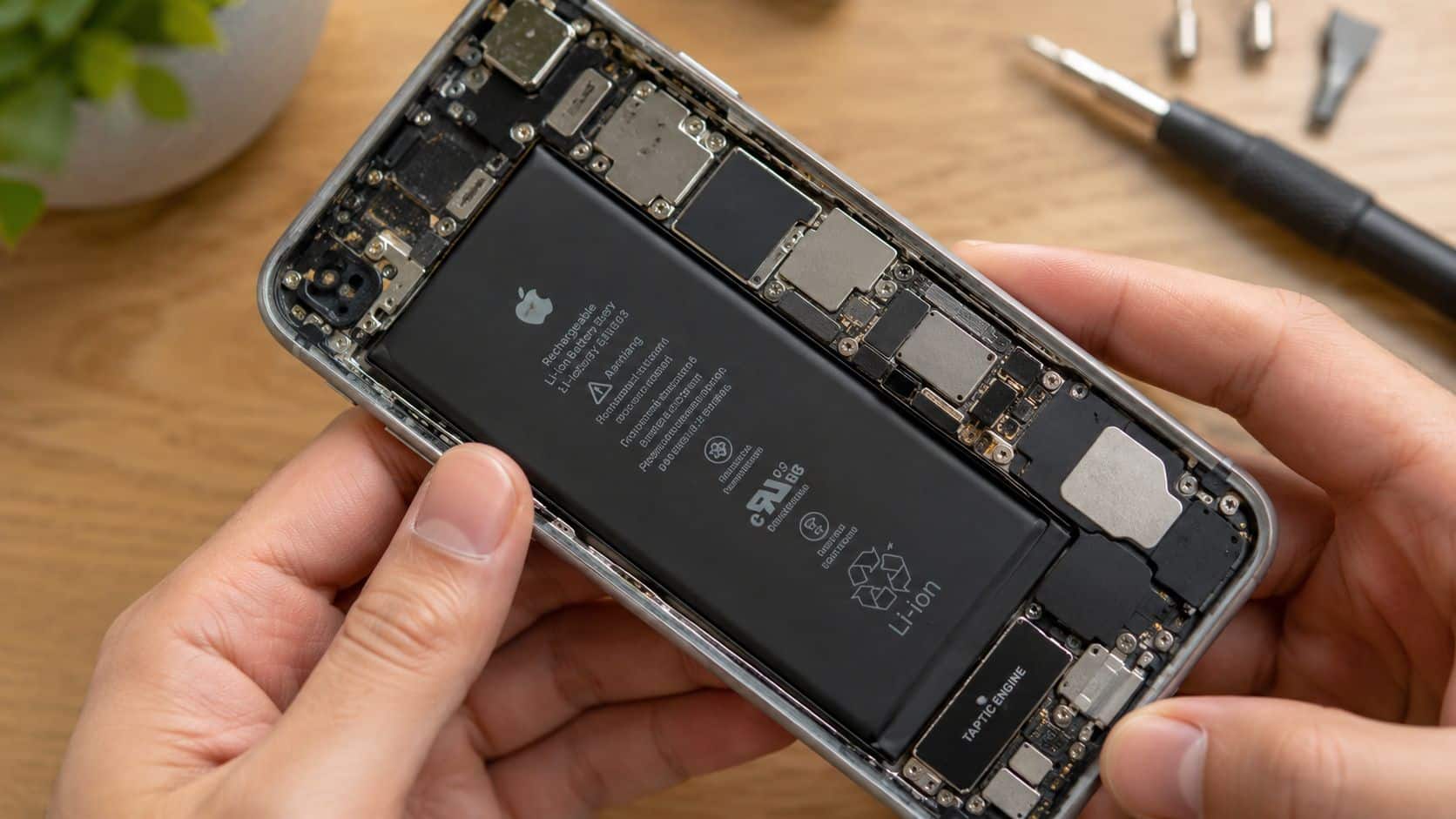 Common Issues with Refurbished iPhones: A UK Buyer's Guide 2 A technician opening an iPhone to reveal the battery and internal hardware components during a repair process.